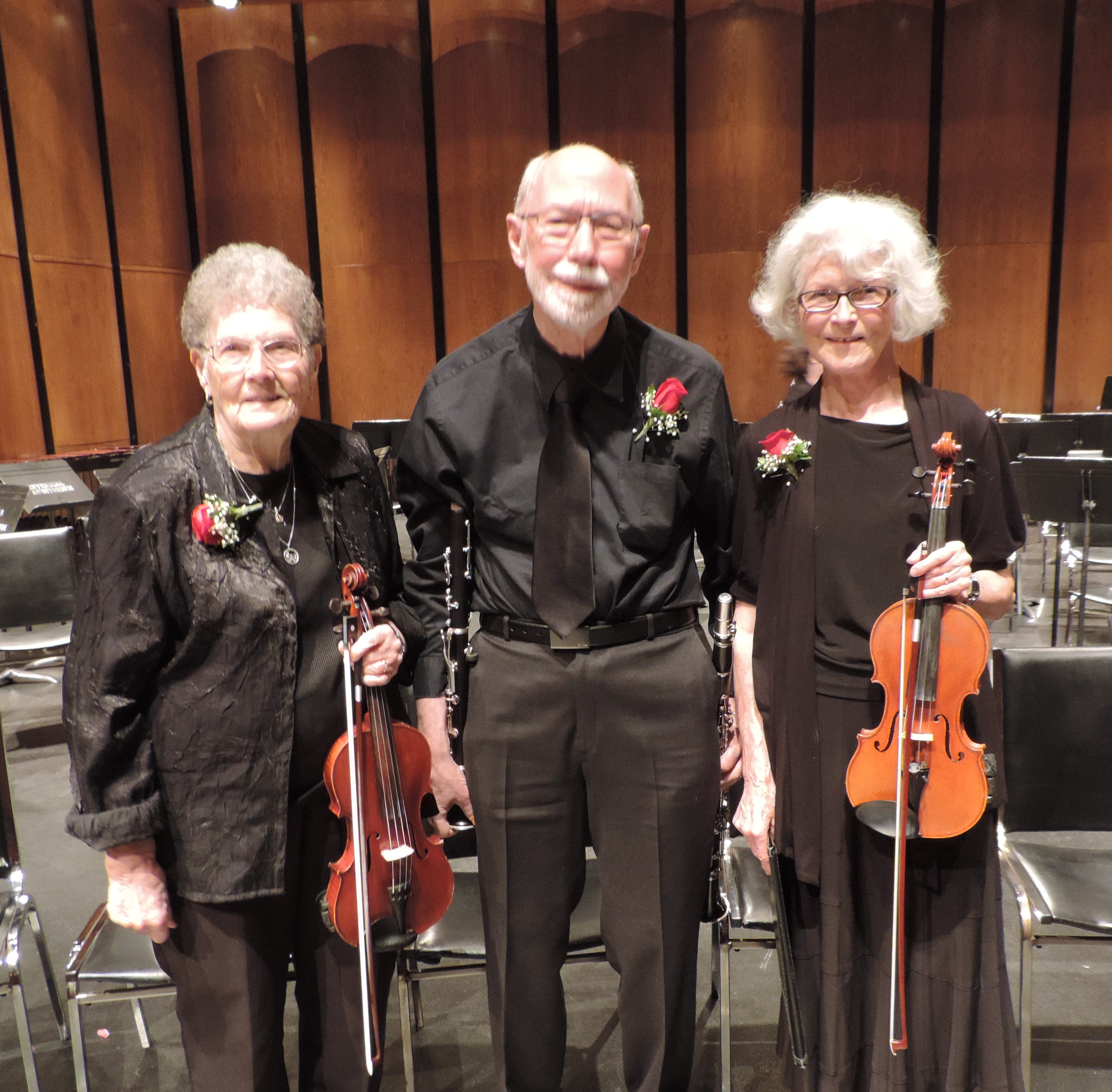Three musicians pose together, dressed in black wearing corsages. They are Erma Wyness and Gwyn Pickering holding violins, and Mel Roberts holding a clarinet. 